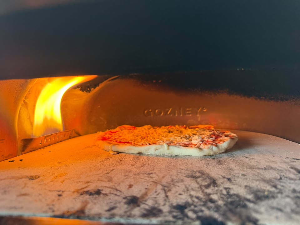Pizza cooking beside a glowing flame